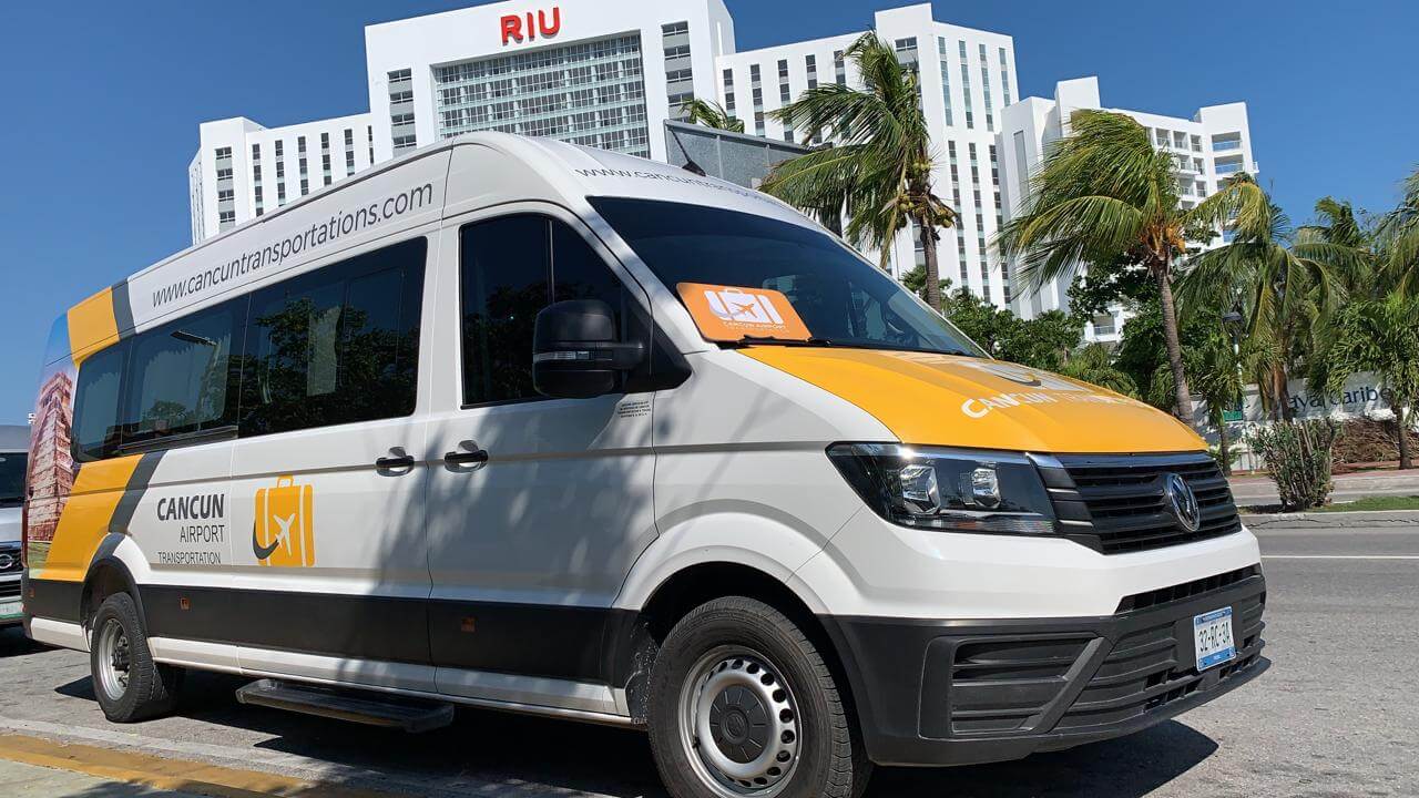 Large van for Group Transportation parked in front of Riu Cancun with board on the window 
