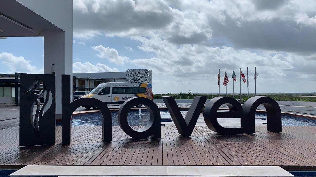Espaciosa van estacionada detrás de letras del hotel Haven Resort durante día nublado