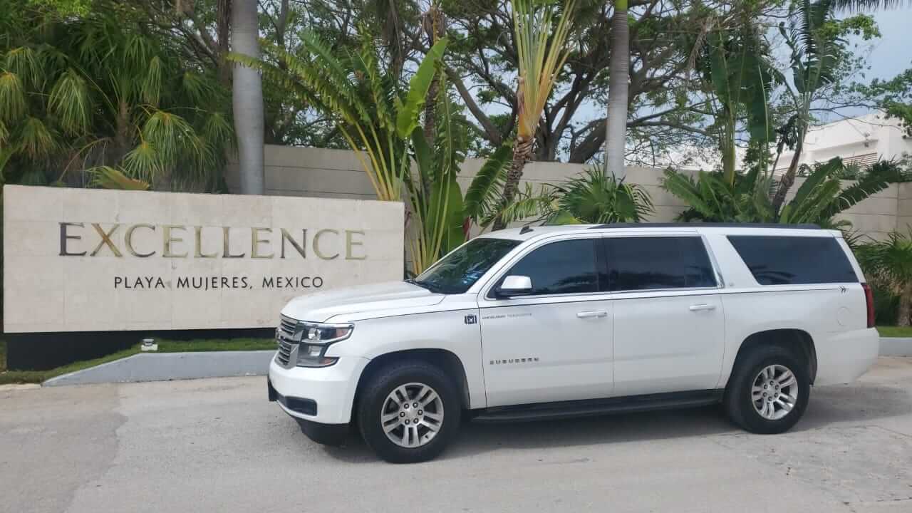 Camioneta de lujo blanca estacionada cerca de letrero de Excellence Playa Mujeres Resort 